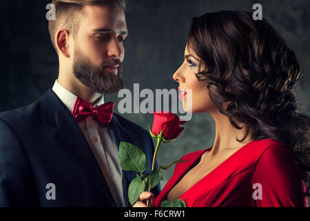 Junge elegante Paar im Abendkleid Portrait. Frau in rot hält Rose und Blick auf den Menschen. Frau im Mittelpunkt. Stockfoto