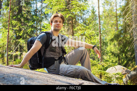 Junger Mann Touristen sitzen auf Stein im Sommer Wald. Stockfoto