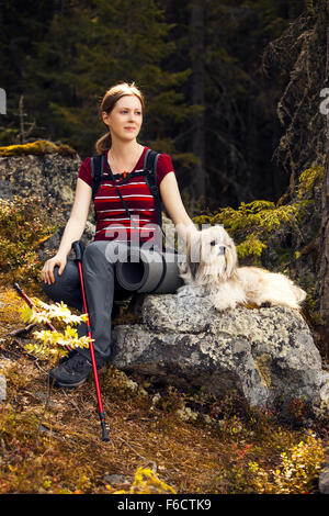 Junge Frau Touristen sitzen auf Stein mit Hund im herbstlichen Wald. Stockfoto