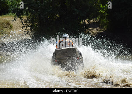 Der Mann auf dem ATV kreuzt einen Stream. Touristischen Spaziergänge auf einem cross-country Gelände. Stockfoto