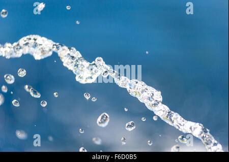 Abstrakte close-up von beleuchteten Wasserstrahl fallen in Fokus gegen verwackelte blauen Hintergrund. Stockfoto