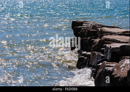 Beleuchtete Kabbelwasser Wellen Spritzen gegen die Kante von felsigen breakwall. Stockfoto