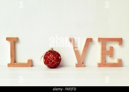 einige Holzbuchstaben und eine rote Weihnachtskugel bilden das Wort Liebe auf eine weiße Szene Stockfoto