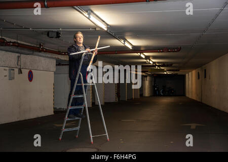 Hausmeister ändert eine Leuchtstofflampe in eine Tiefgarage zur Verfügung. Stockfoto