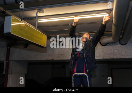 Hausmeister ändert eine Leuchtstofflampe in eine Tiefgarage zur Verfügung. Stockfoto