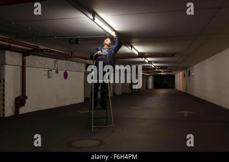 Hausmeister ändert eine Leuchtstofflampe in eine Tiefgarage zur Verfügung. Stockfoto