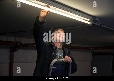 Hausmeister ändert eine Leuchtstofflampe in eine Tiefgarage zur Verfügung. Stockfoto