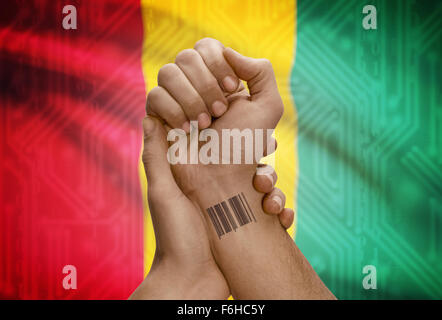 Barcode-ID Nummer Tätowierung am Handgelenk der dunkle enthäutete Person und Nationalflagge auf Hintergrund - Guinea Stockfoto