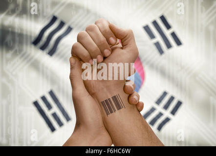 Barcode-ID Nummer Tätowierung am Handgelenk dunkle enthäutete Person und Nationalflagge auf Hintergrund - Südkorea Stockfoto