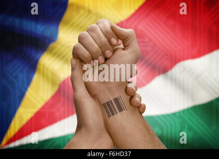 Barcode-ID Nummer Tätowierung am Handgelenk der dunkle enthäutete Person und Nationalflagge auf Hintergrund - Seychellen Stockfoto