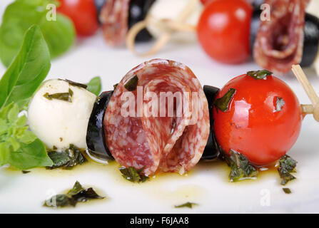 Vorspeise von Salami mit Mozzarella, Oliven, Kirschtomaten am Spieß mit Basilikumöl Stockfoto