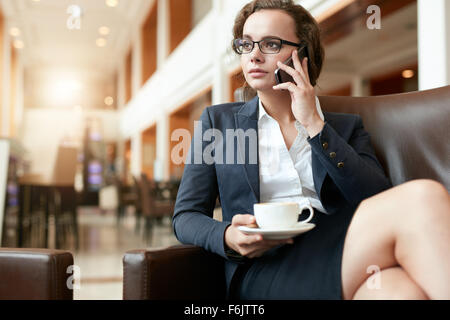 Porträt der Geschäftsfrau im Coffee Shop mit Handy sitzen. Weibliche Führungskraft mit Tasse Kaffee am Handy sprechen. Stockfoto