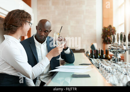 Zwei junge Geschäftsleute Toasten Getränke im Café. Afrikanischen Geschäftsmann mit kaukasischen Partnerin ein Glas Getränk an Stockfoto