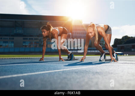 Zwei weibliche Athleten in Ausgangsposition bereit, ein Rennen zu starten. Sprinter bereit für Rennen auf der Rennstrecke mit Sonne Flare. Stockfoto