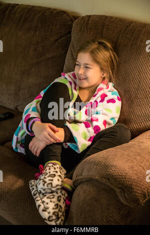 Zehn Jahre altes Mädchen in Robe und Pyjamas, die sitzen auf dem Sofa vor dem Fernseher in Issaquah, Washington, USA Stockfoto