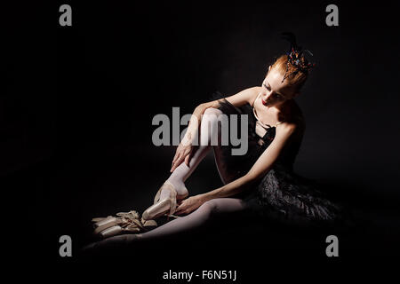 Schlanke Tänzerin in ein schwarzes Korsett und schwarzen Tutu Spitzenschuhe binden. Klassisches Ballett. Fotografie in zurückhaltend. Stockfoto