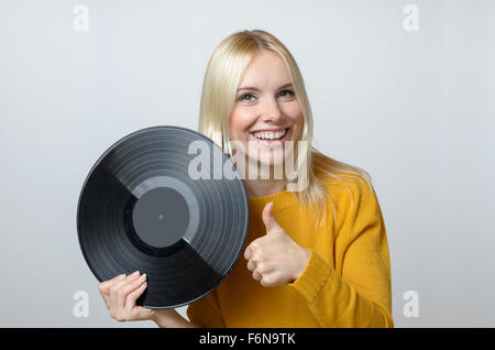 Eine halbe Stelle erschossen von eine glückliche junge Frau hält eine Schallplatte und Daumen in die Kamera vor weißem Hintergrund auftauchen. Stockfoto