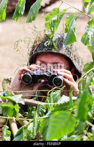 Weltkrieg zwei Re-enactment. Der Leiter der Deutschen Wehrmacht Officer, teilweise hinter Laub versteckt, Blick durch ein Fernglas. Kein Auge - Kontakt. Stockfoto