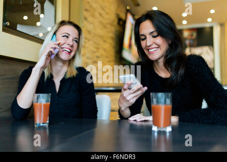 Zwei schöne Frauen telefonieren im Café während glücklich zu sein Stockfoto