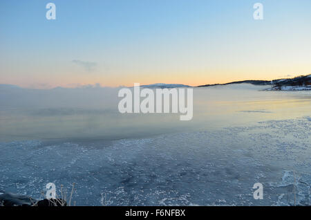 schöne dicke Eisnebel über kalten Fjord Wasser mit bunten Sonnenuntergang Himmel Stockfoto