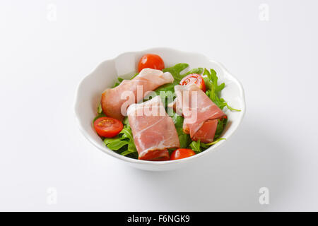 Schüssel mit getrockneten Schweinefleisch Schinken, Rucola und Spinat Blätter und halbierte Kirschtomaten auf weißem Hintergrund Stockfoto