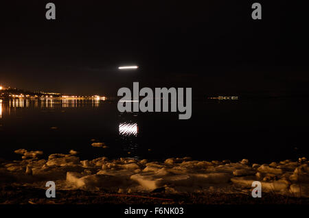 lange helle Streifen nach der Landung Flugzeug Reflexion auf ruhigen Fjord Wasseroberfläche mit Stadt und Lichter im Hintergrund Stockfoto