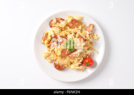 Teller mit Rührei mit Zwiebel und in Scheiben geschnittene Wurst auf weißem Hintergrund Stockfoto