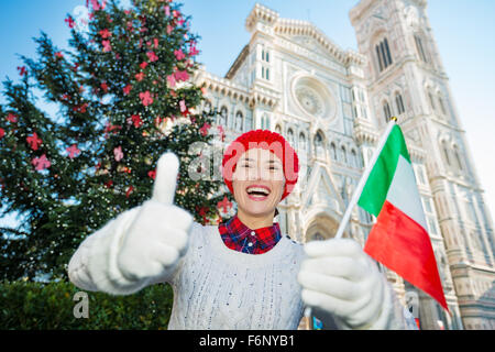 Daumen hoch für Weihnachten in Florenz! Glückliche Reisende Frau mit italienischer Flagge stand vor traditionellen Weihnachtsbaum in der Nähe von Dom während Ausgaben Spaß Zeit in Florenz, Italien Stockfoto