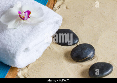 Schwarzen Sie Basaltsteinen, weißes Handtuch, Orchidee Blume, Aqua lackiertem Holz auf Sand Hintergrund.  Nahaufnahme, Exemplar, selektiven Fokus Stockfoto