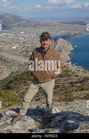 Reifer Mann posiert mit Händen in den Hosentaschen auf Sokol Berg im Panorama der östlichen Krim-Küste-Hintergrund in Richtung S Stockfoto