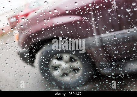 Nassen Sie Autofenster mit Regentropfen und ein verschwommenes Auto hinter. Nahaufnahme Foto mit Tiefenschärfe und flachen DOF Stockfoto