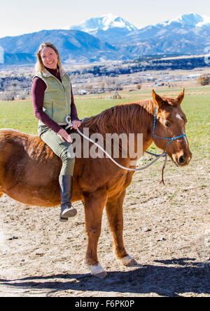 Attraktive Frau Reiten ohne Sattel auf der Ranch Weide mit Rocky Mountains im Hintergrund Stockfoto
