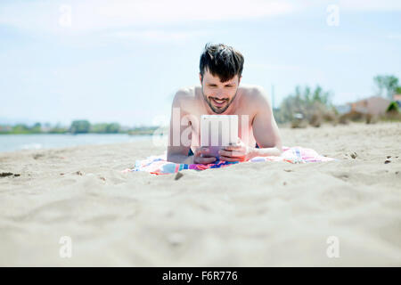Junger Mann mit digital-Tablette am Strand Stockfoto