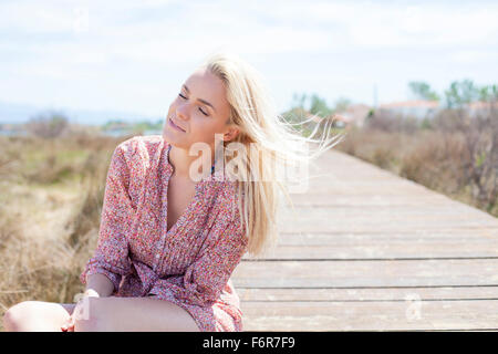 Junge Frau sitzt auf Promenade Augen geschlossen Stockfoto