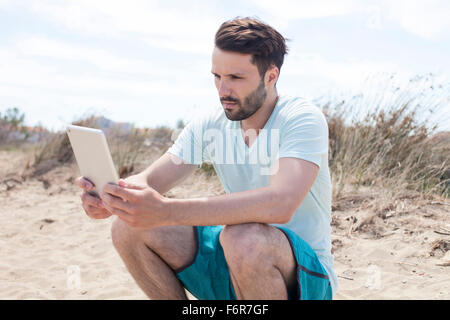 Junger Mann mit digital-Tablette am Strand Stockfoto