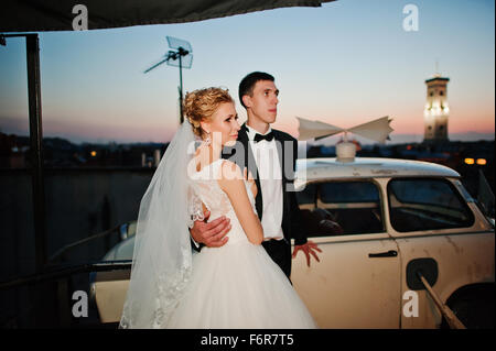 Hochzeitspaar auf dem Dach des Gebäudes in Abend mit Retro-Auto Stockfoto