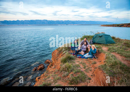 Gruppe von Freunden sitzen auf Campingplatz am Rand des Wassers Stockfoto