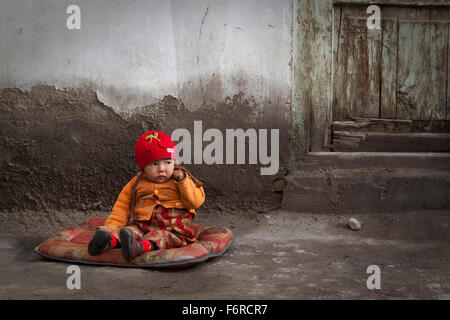 Uigurisches Mädchen, das vor dem Haus sitzt, Yengisar, Autonome Region Xinjiang, China. Stockfoto