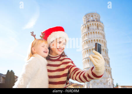 Glückliche Mutter in Weihnachtsmütze und Tochter tragen lustige Rentier-Geweih unter Selfies vor schiefen Pisa, Italien-Rundfahrt Stockfoto