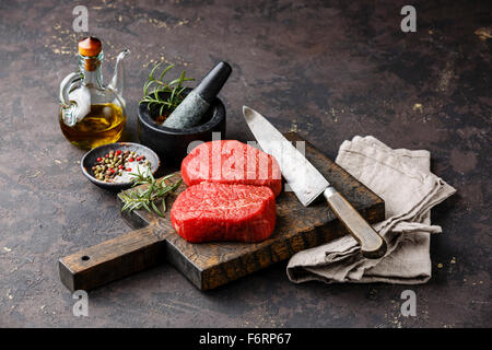 Rohe marmorierte Frischfleisch Steaks mit Gewürzen und Küchenmesser auf dunklem Hintergrund Stockfoto