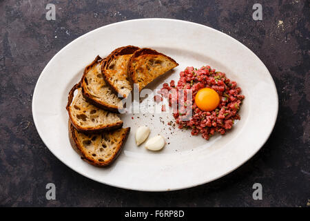 Rindertatar mit Gewürzgurken und Toasts auf weißen Teller auf dunklem Hintergrund Stockfoto