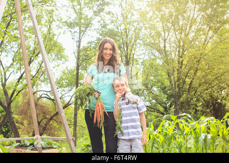 Kaukasische Mutter und Sohn halten Karotten im Garten Stockfoto