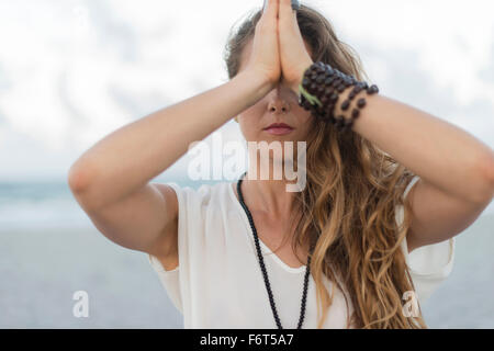 Hispanic Frau meditieren am Strand Stockfoto