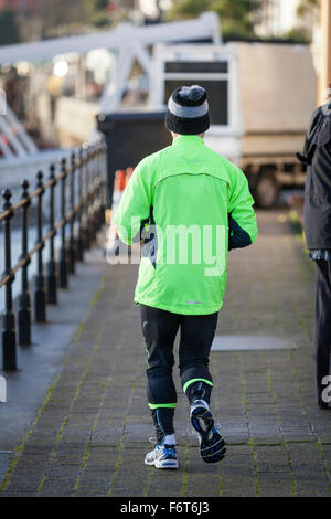 Ein älterer Mann trägt eine wollige Pudelmütze, läuft Trainingsanzug Hose und einem grünen hi-viz Spitze weg von der Kamera auf die Docks in Stockfoto