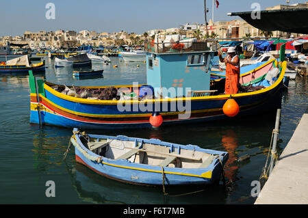 Maltesische Fischer arbeiten auf eine bunte Luzzu, einem traditionellen Fischerboot im Hafen von Marsaxlokk, Malta Stockfoto