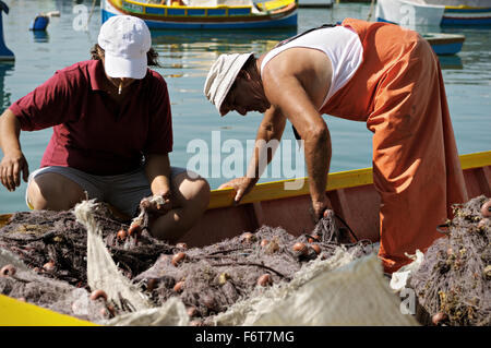 Zwei Fischer arbeiten mit Fischernetzen auf einem Boot im Hafen von Marsaxlokk, Malta Stockfoto