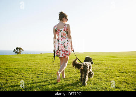 Kaukasische Frau zu Fuß Hund im Feld Stockfoto