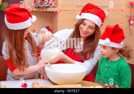 Mutter mit zwei niedlichen Kinder backen in der Küche zu Hause tragen rote Nikolausmütze, so dass traditionelle Weihnachts-Zubereitung Stockfoto