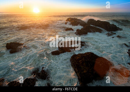 Meer Surfen auf den Felsen bei traumhaften Sonnenuntergang. Stockfoto