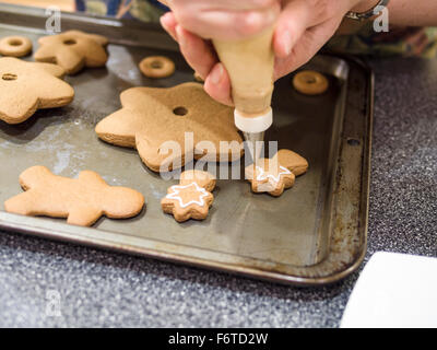 Sahnehäubchen abgeschlossen Lebkuchen Stücke. Eine Frau Rohre Puderzucker auf den Rändern der ein Lebkuchen-Stück für einen Weihnachtsbaum Stockfoto